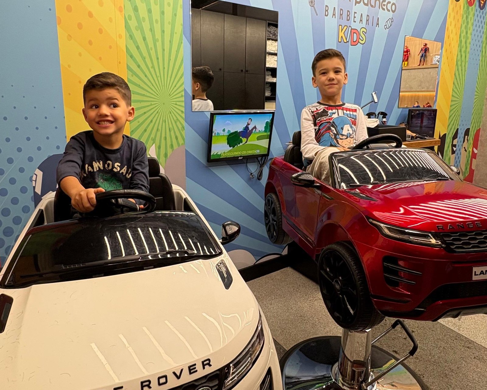 Crianças na área kids da Maicon Pacheco Barbearia, em cadeiras temáticas de carrinho, em Joinville